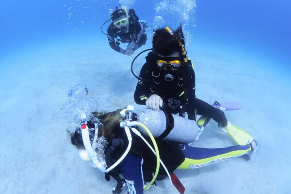 水中で女性のボンベを点検するインストラクター